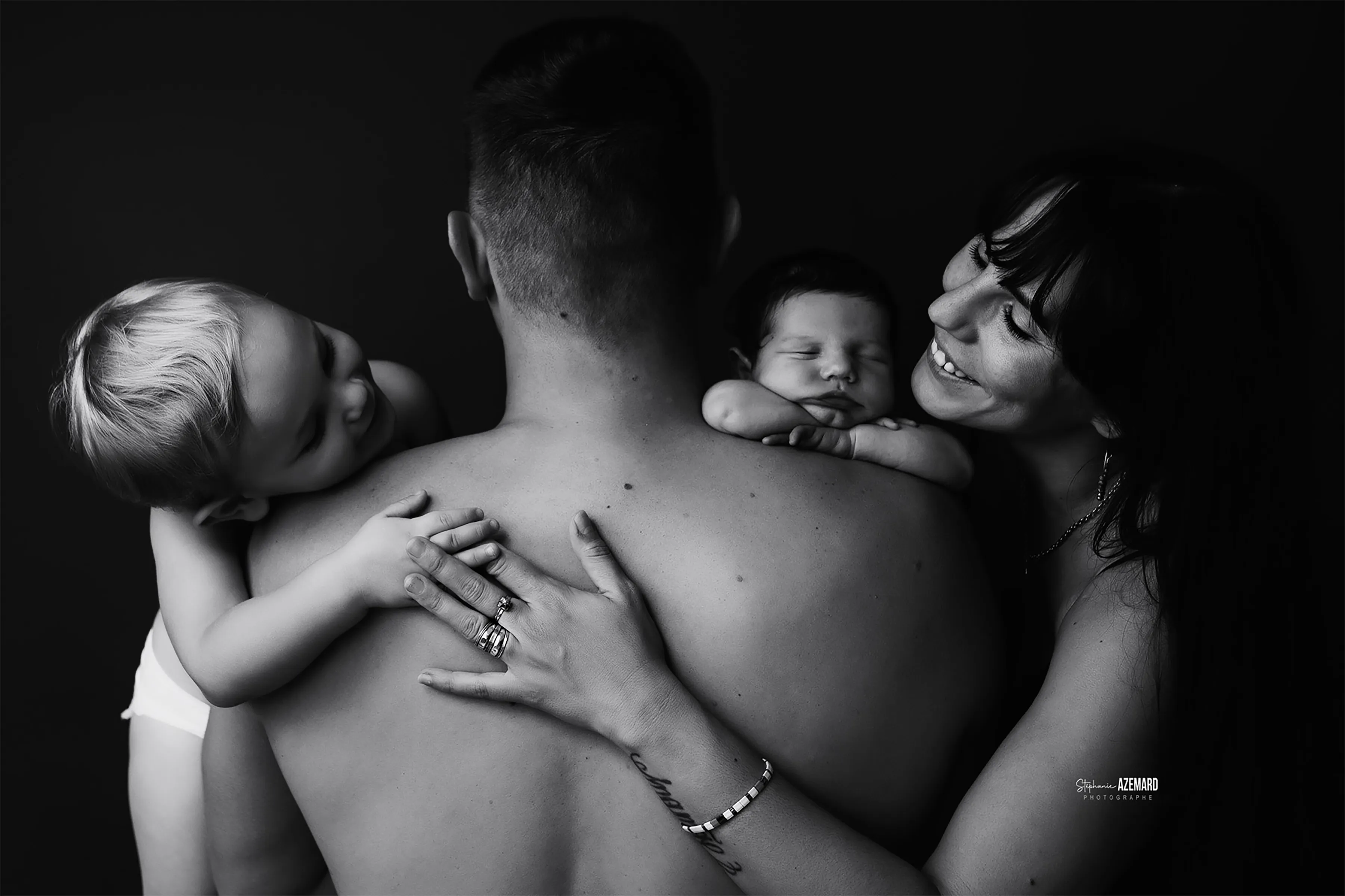 Photo famille parents avec nouveau-né endormi et grand enfant blond en noir et blanc studio, photographe maternité Montpellier Stéphanie Azémard